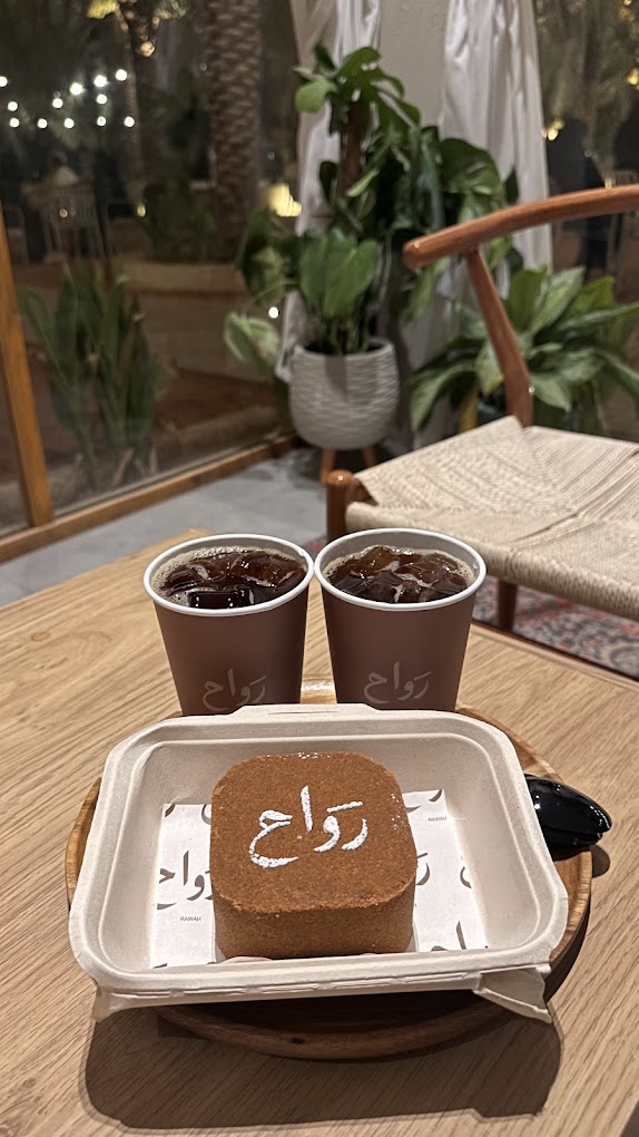 Two iced coffees in rawah cups next to a slice of cake